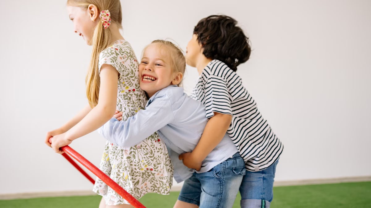 Three children joyfully play indoors with a hula hoop, showcasing happiness and togetherness.